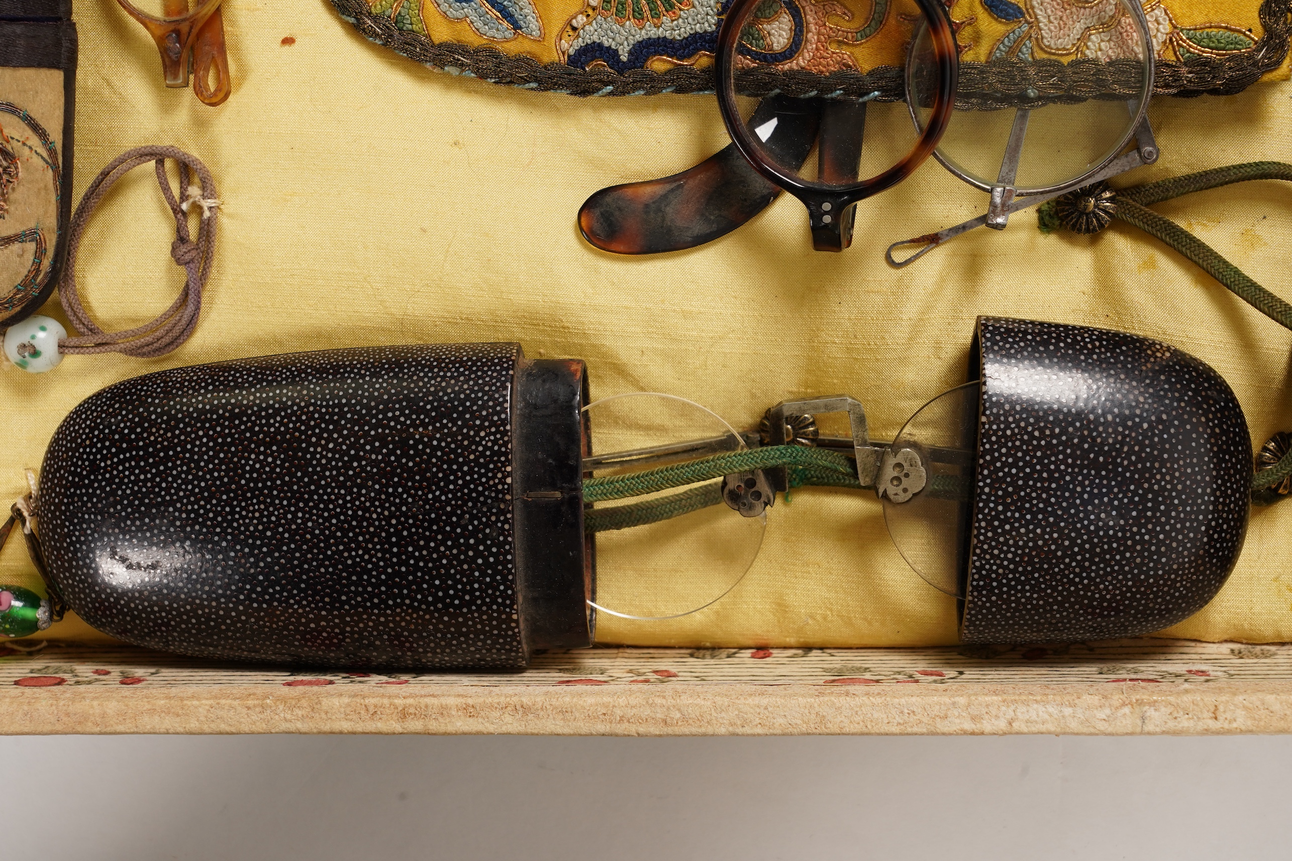 A collection of 19th/20th century Chinese embroidered silk spectacle cases and various spectacles, Box 33cm square